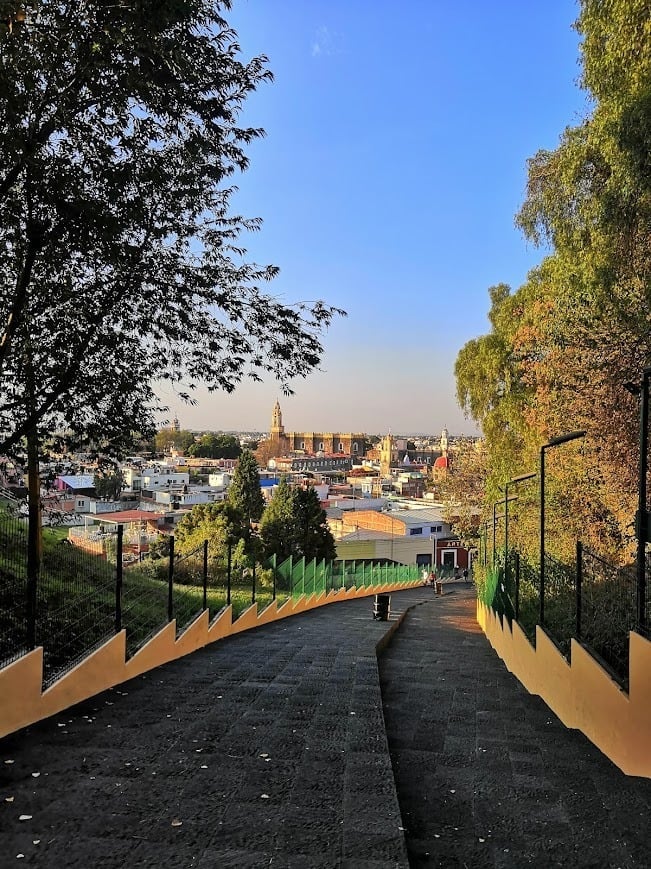Modern paved pathway lined with trees overlooking Puebla historic cathedral colorful buildings
