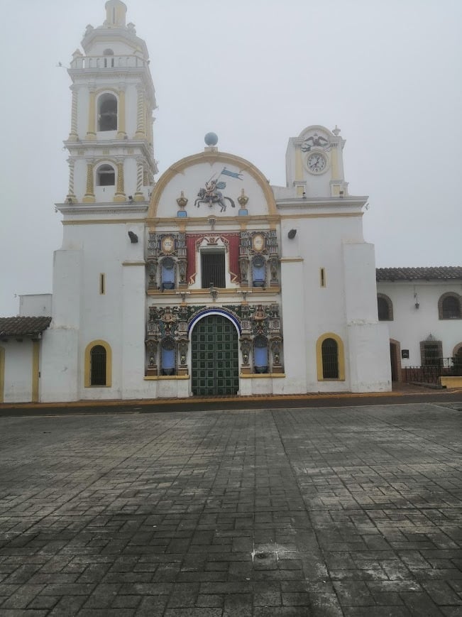 White Spanish colonial church with bell tower dome and green doors facing empty plaza in Puebla