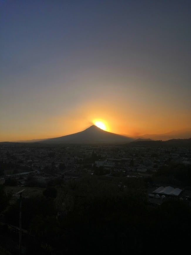 Dramatic sunset with conical volcano silhouette against golden sky, urban landscape at dusk