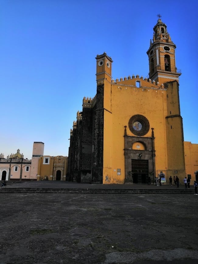 Bright yellow colonial church with twin bell towers in Puebla Mexico plaza under blue sky